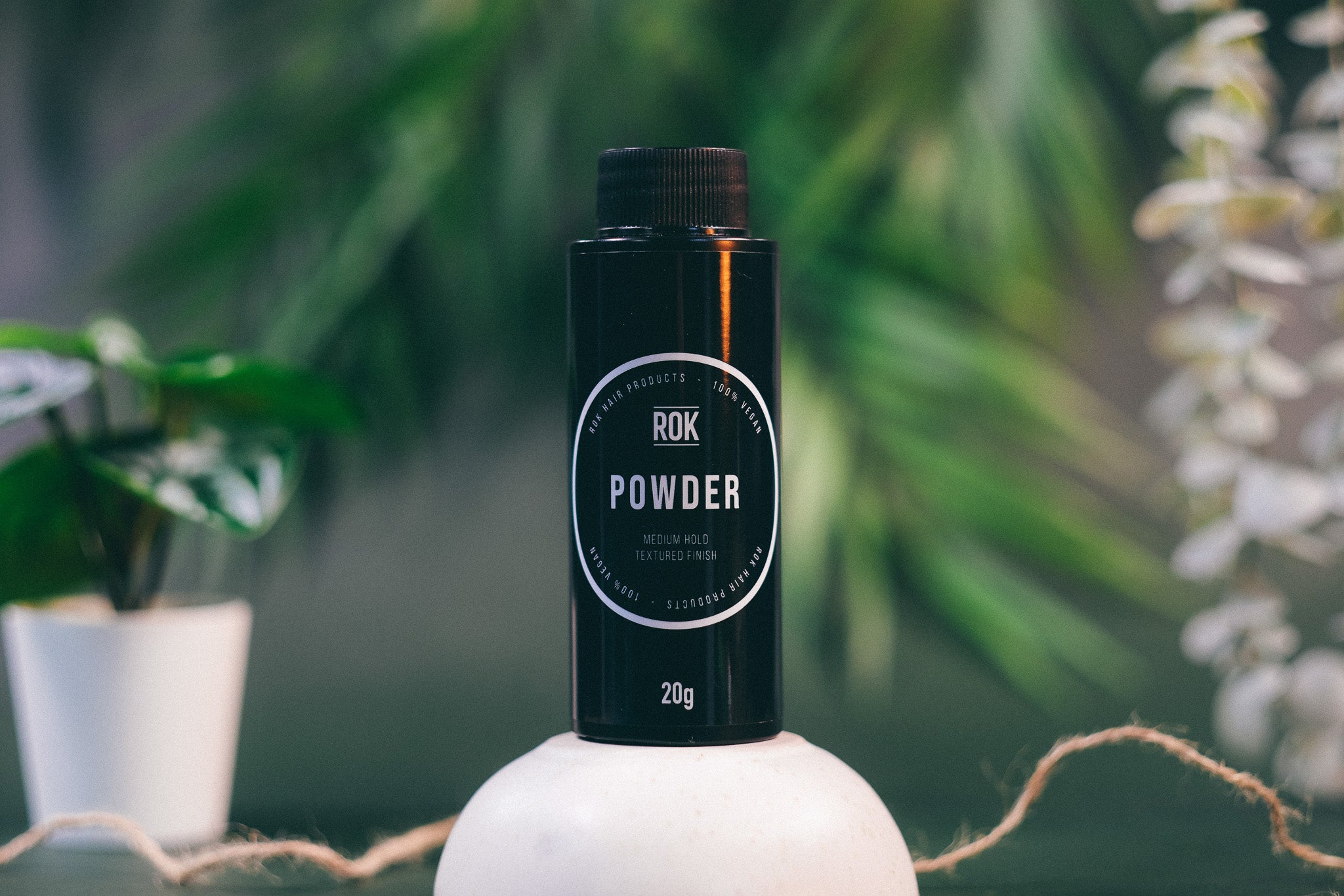 ROK Powder black bottle on white stand with tropical plant background – vegan hair powder UK