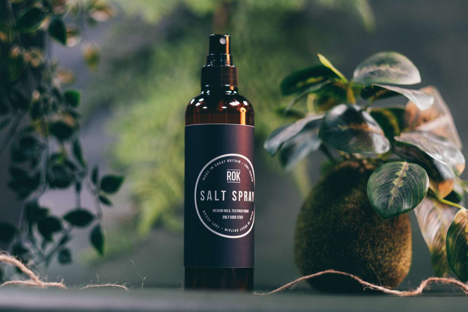 ROK Salt Spray bottle with large tropical leaf and rope on dark background – beach wave hair spray