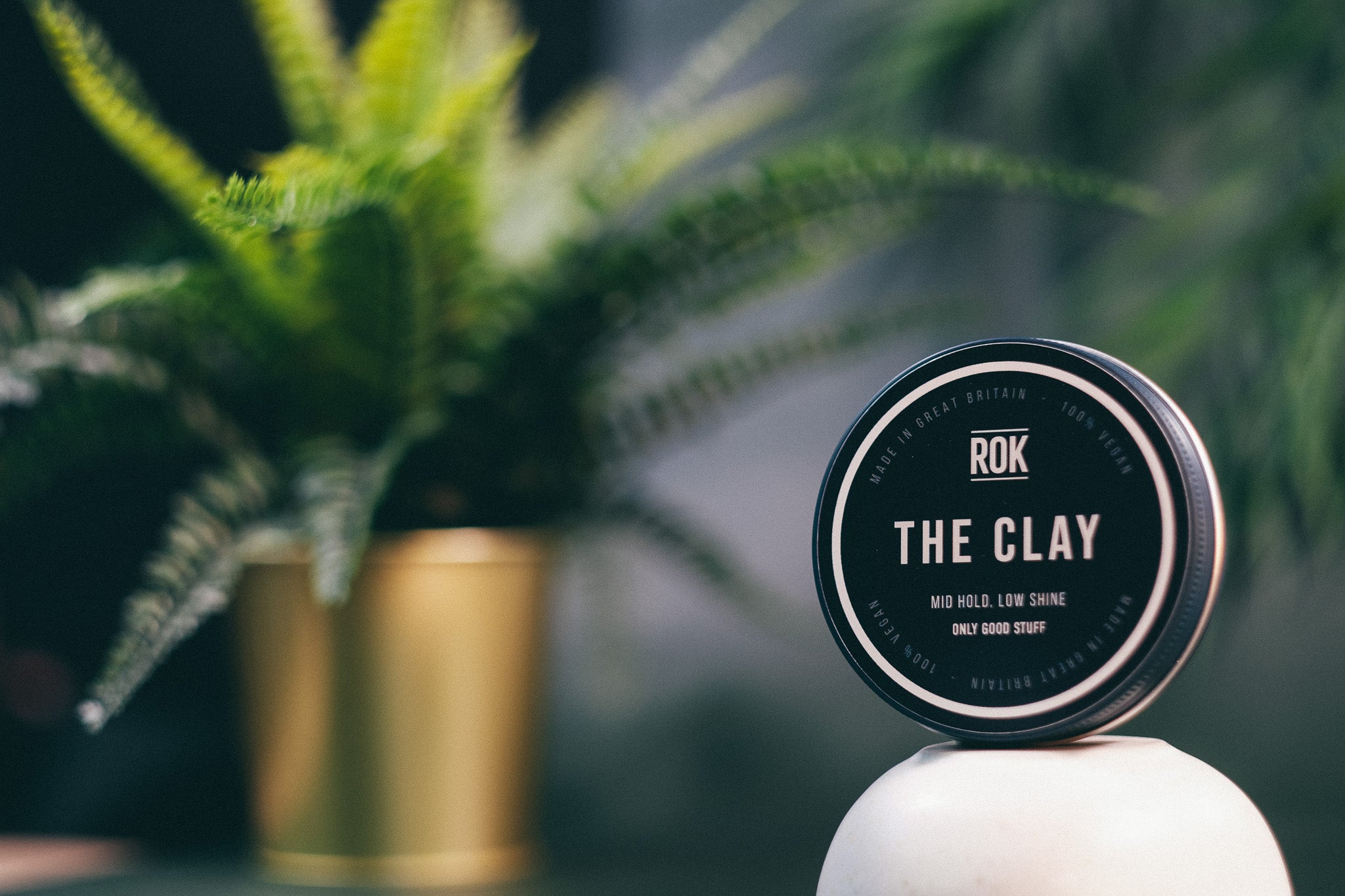 ROK The Clay puck on pedestal with plant in background – mid hold low shine hair clay