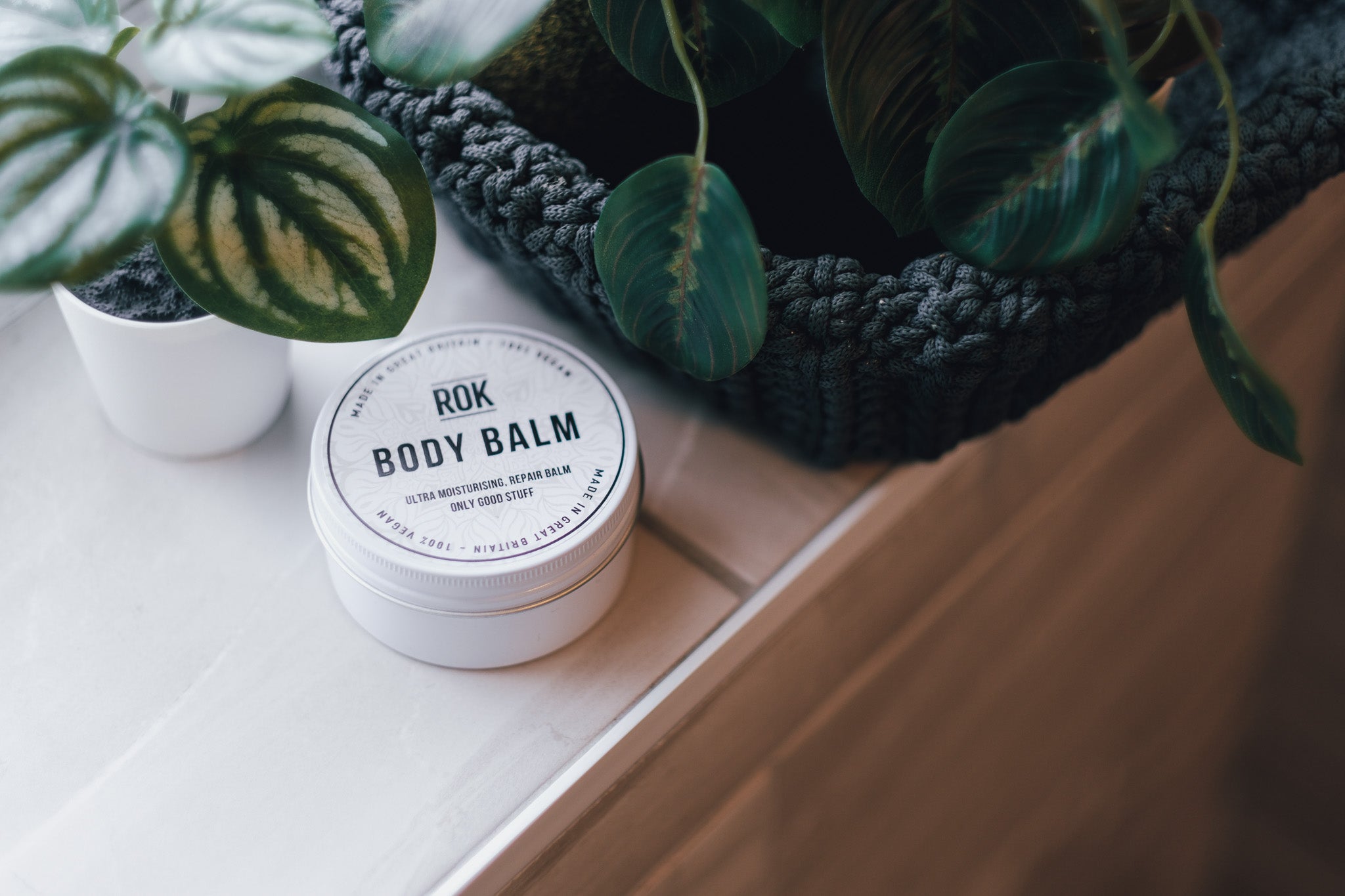ROK Body Balm tin on wooden surface with tropical plant display – vegan repair body balm UK