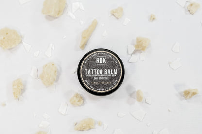 ROK Tattoo Balm tin on white surface with scattered dried botanicals – vegan tattoo aftercare