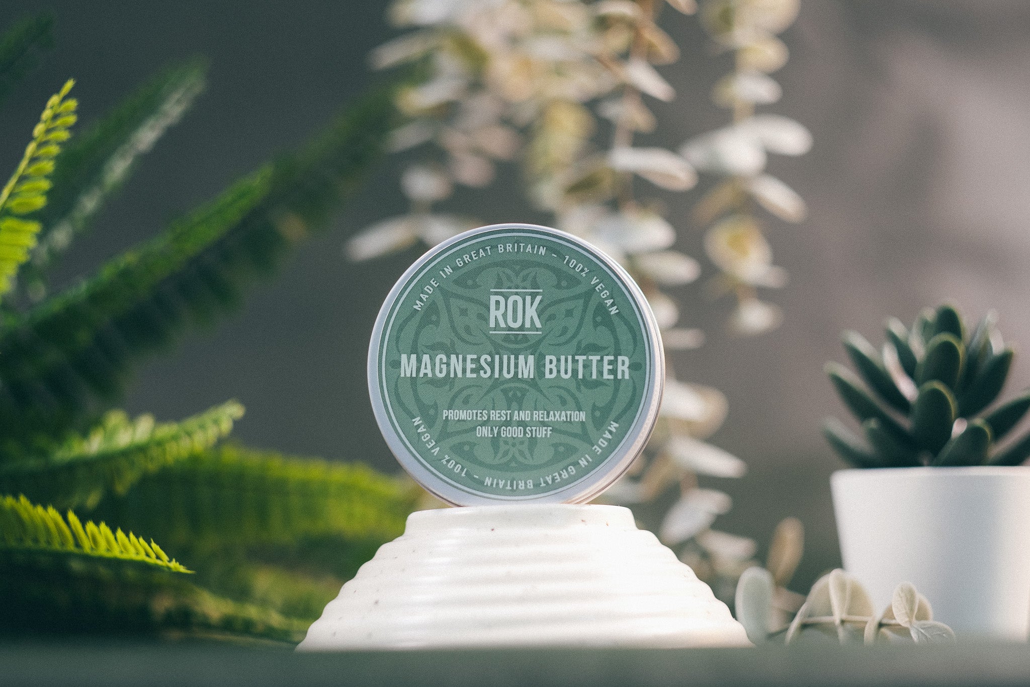 ROK Magnesium Butter tin on white stand with fern plants – relaxing skincare from ROK Products