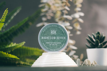 ROK Magnesium Butter tin on white stand with fern plants – relaxing skincare from ROK Products